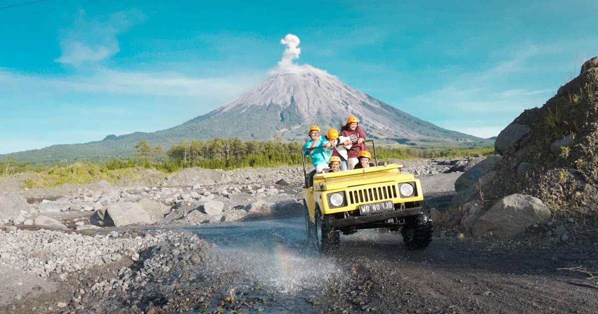 Jeep kuning melintasi jalur berbatu dengan latar Gunung Semeru